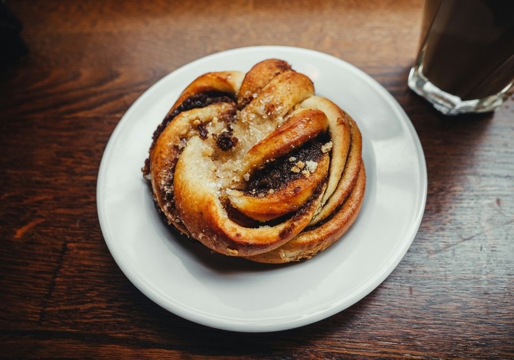 Twisted cinnamon scroll sweet bun on a white plate with coffee