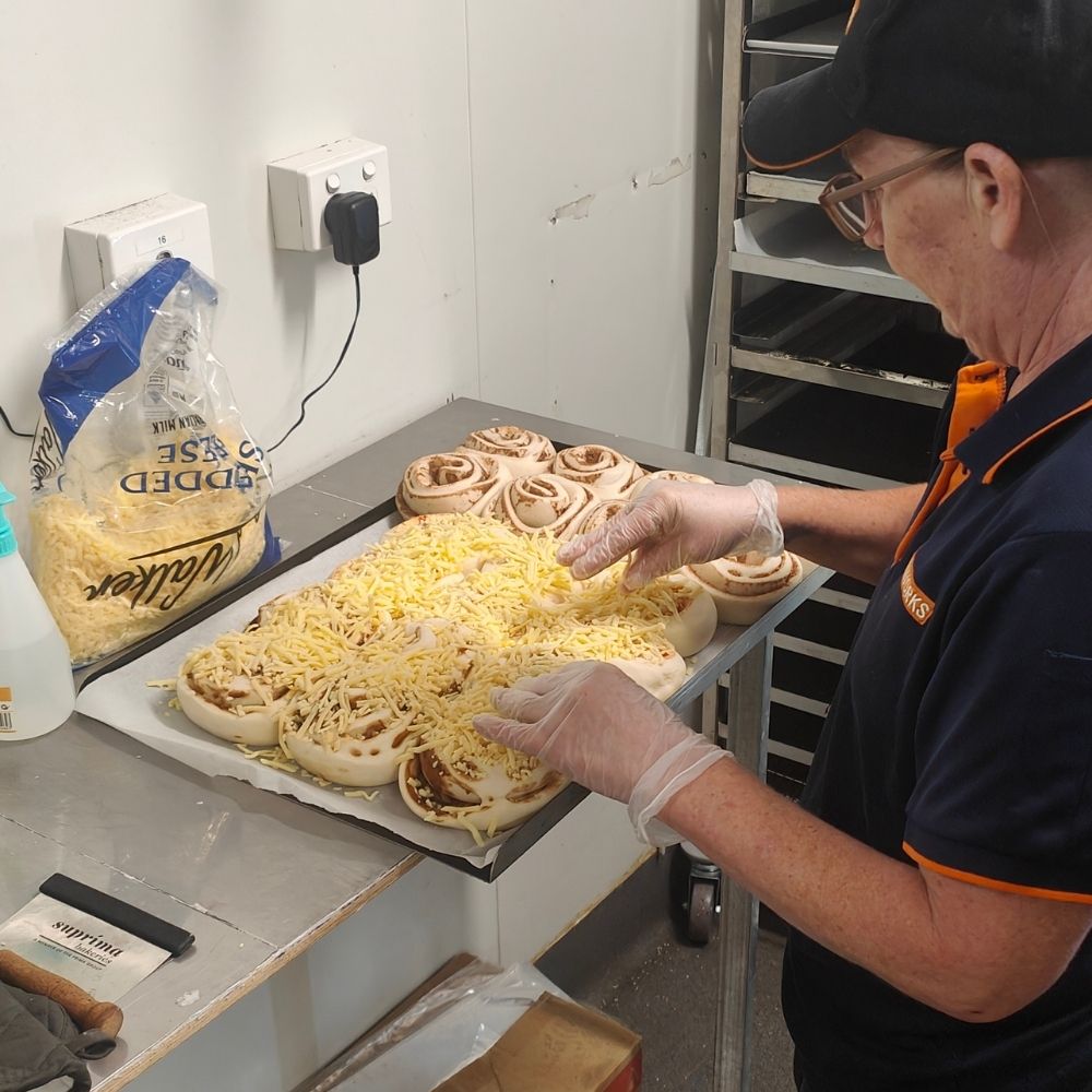 Baker topping Suprima scrolls with cheese before baking at FoodWorks Pottsville